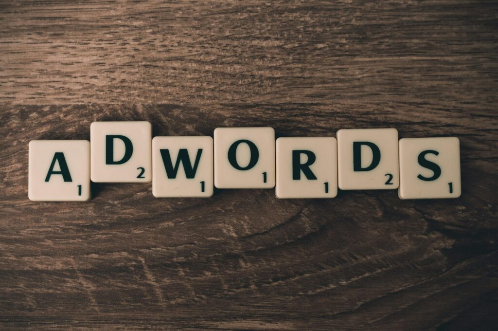 Litery do gry w stylu Scrabble ułożone na drewnianym stole, tworzące słowo „ADWORDS”, symbolizujące wykorzystanie sztucznej inteligencji w marketingu i zarządzanie kampaniami reklamowymi online.